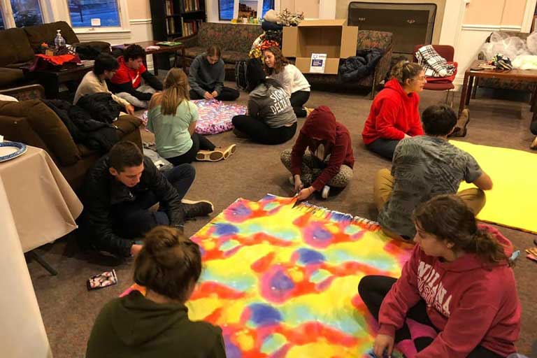 Students work on blankets in fireplace room.